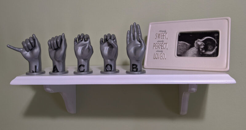 Letters "JACOB" in metallic silver with black letters on a shelf