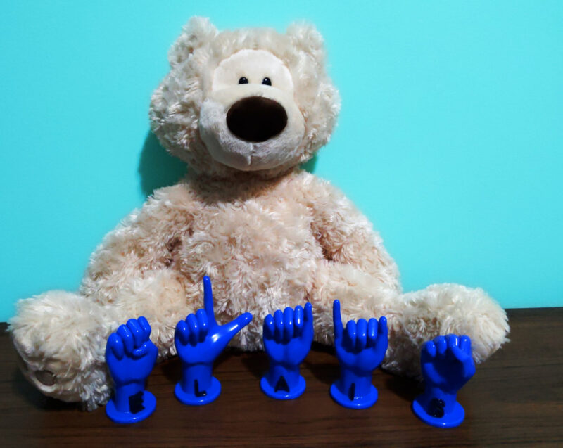 3D Printed ASL Letters "ELIAS" in blue with black letters in front of a stuffed bear